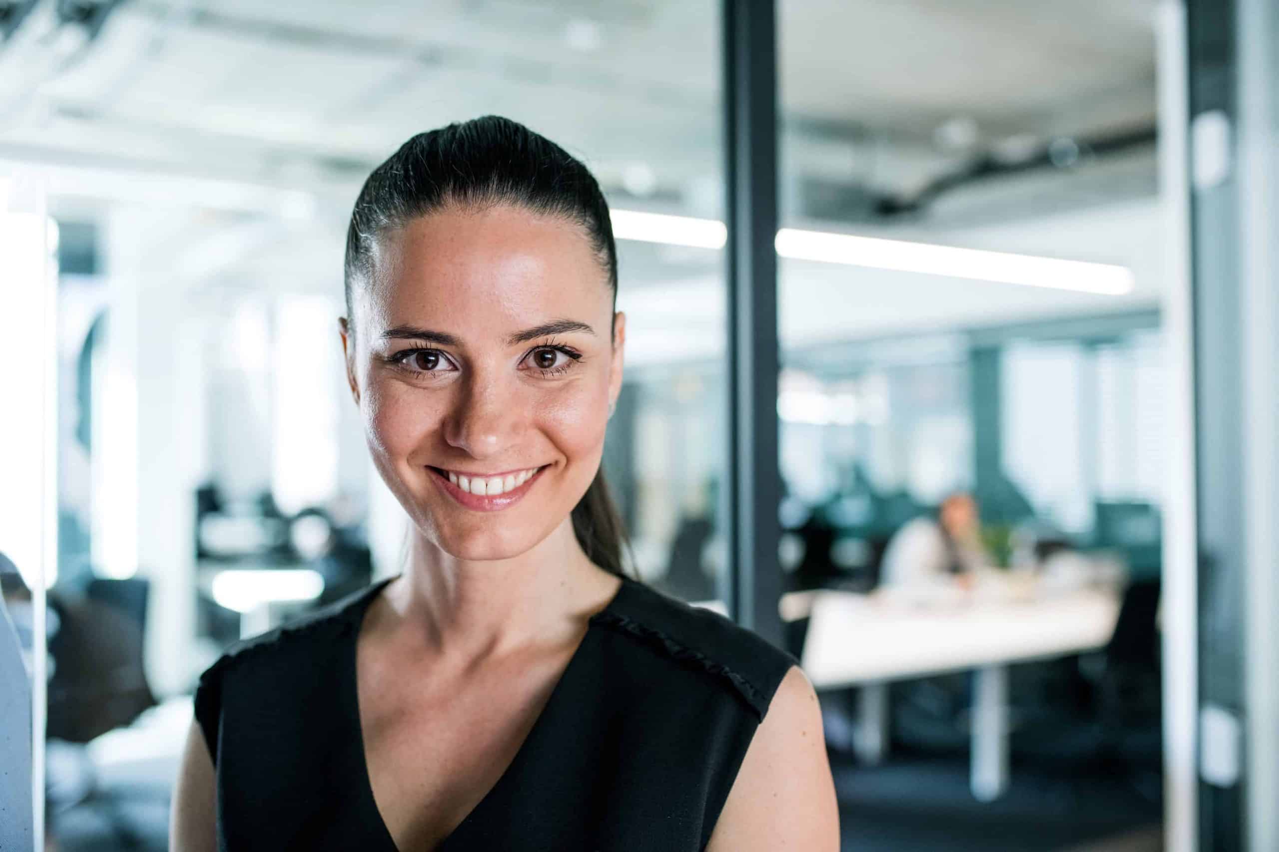 Front view of young businesswoman standing in an office, looking at camera.