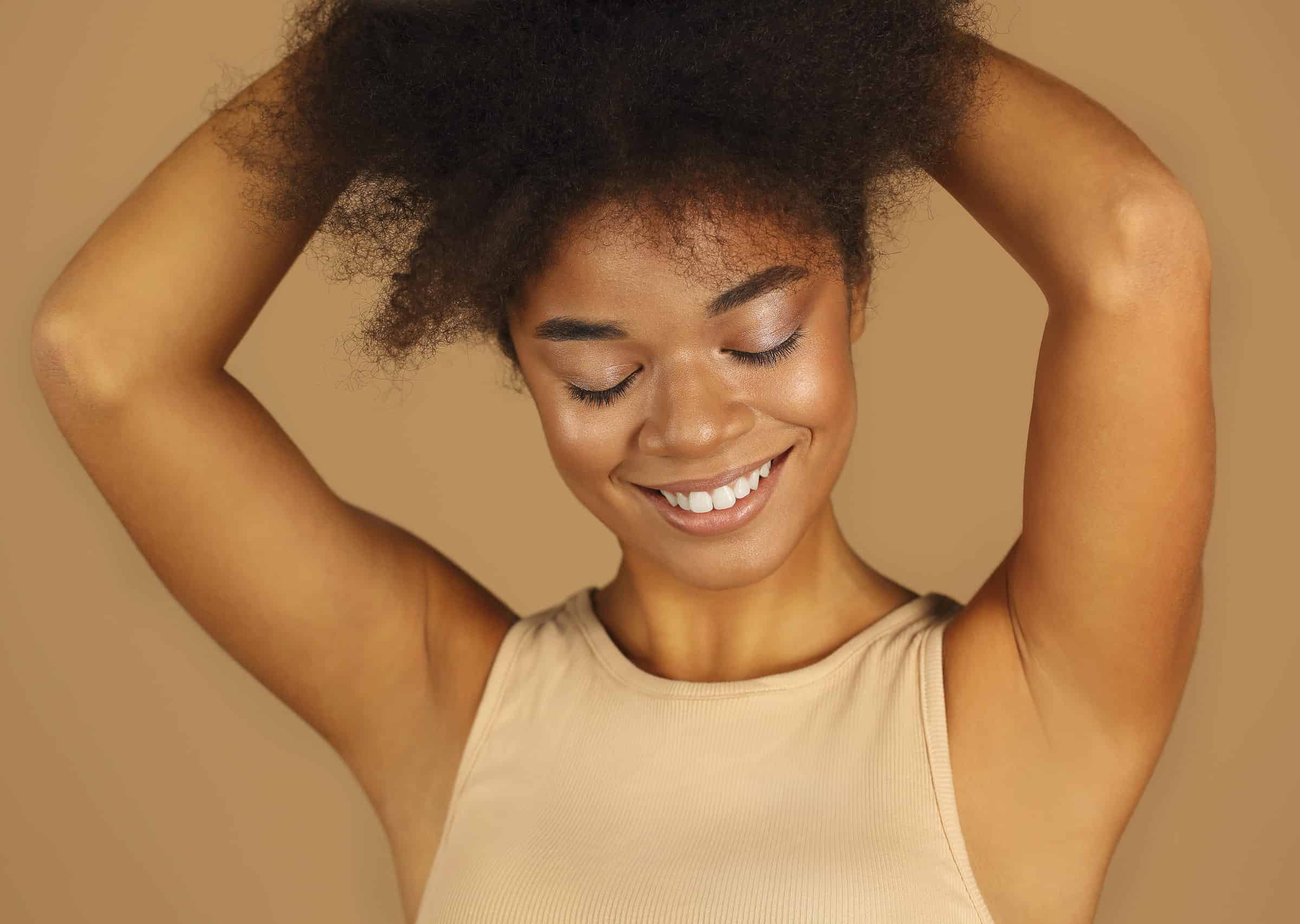 young lovely african american woman with arms raised demonstrating smooth clean armpits without hair