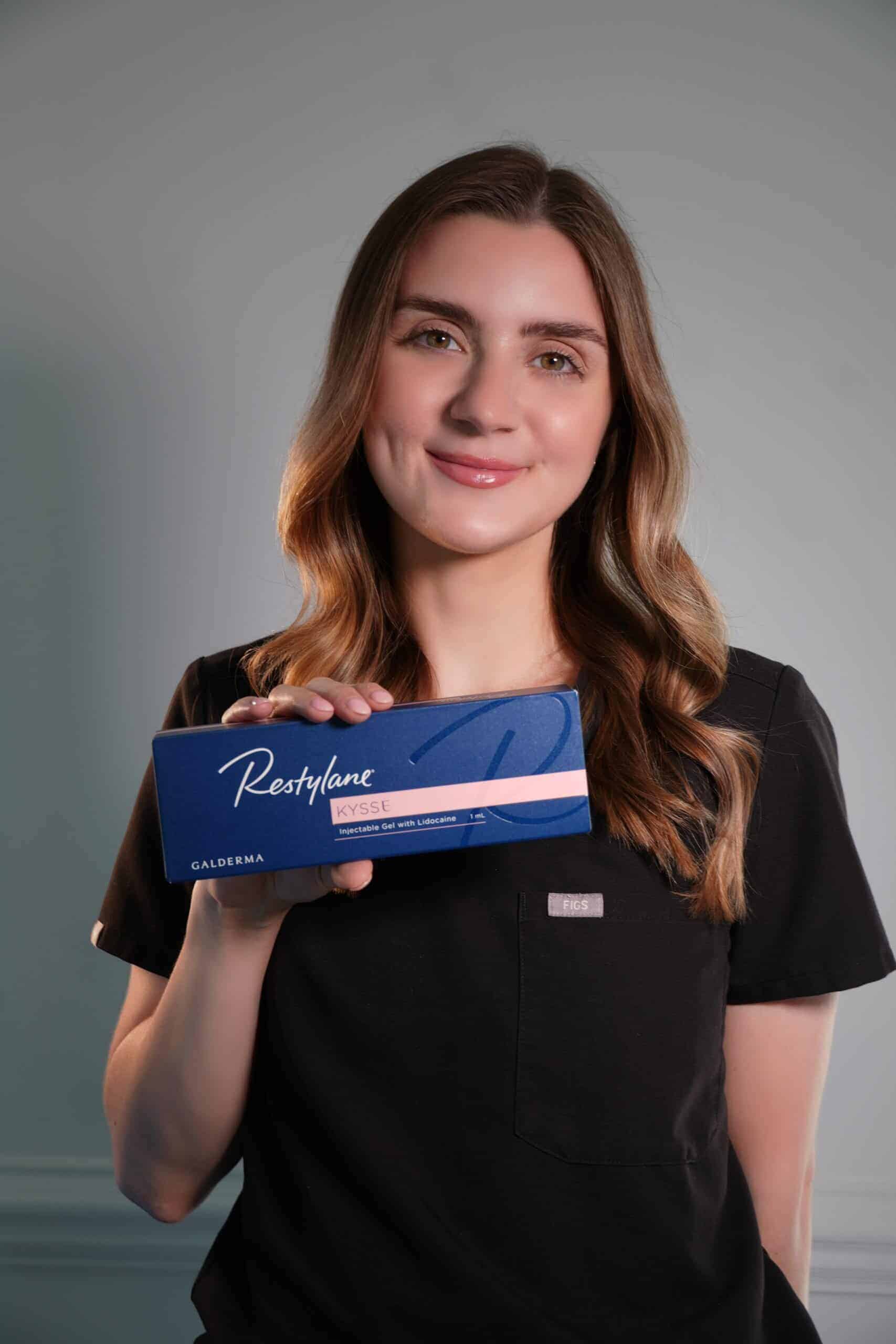 A woman in a black shirt holding a box of pink eye drops]