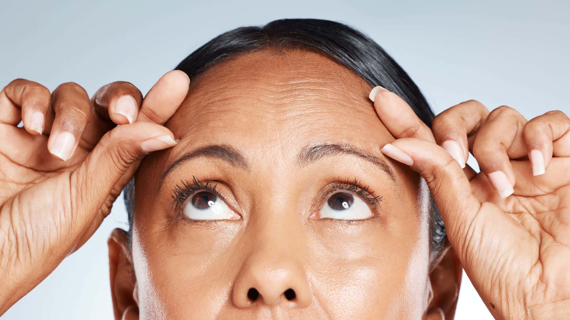Woman examining forehead wrinkles closely.