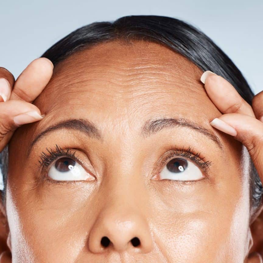 Woman examining forehead wrinkles closely.