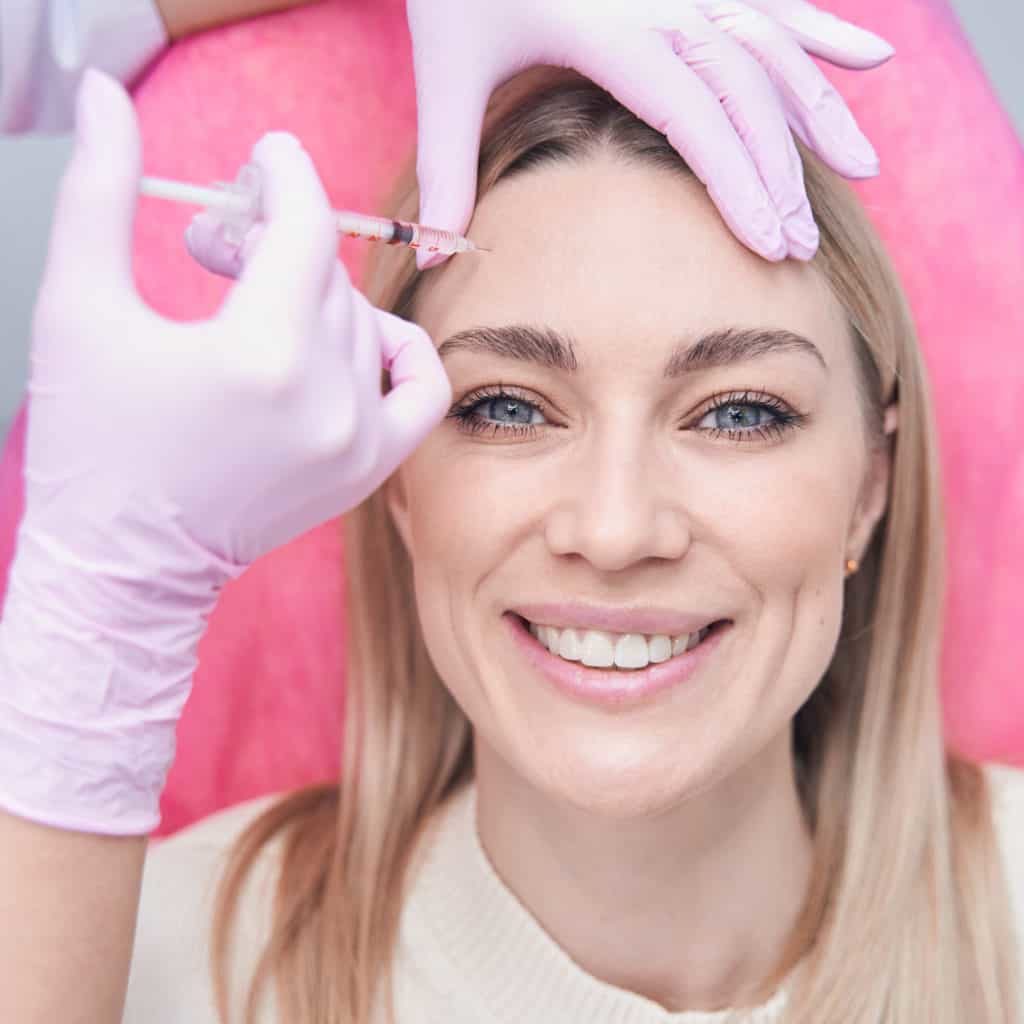 Top view of cheerful young woman looking up during mesotherapy procedure conducted by beautician