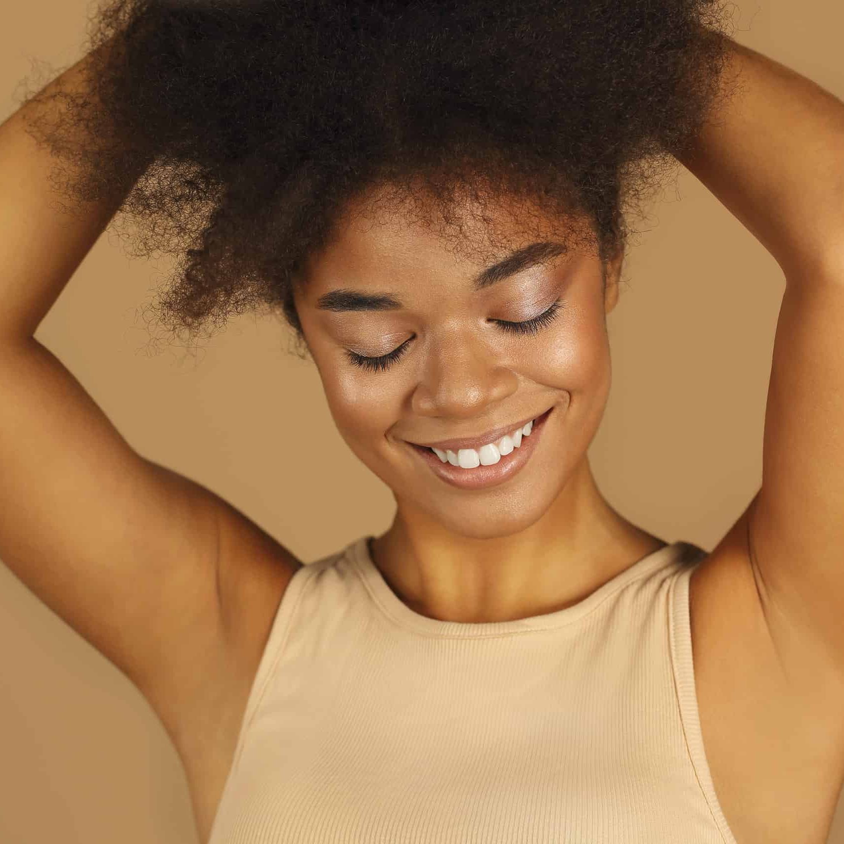 young lovely african american woman with arms raised demonstrating smooth clean armpits without hair